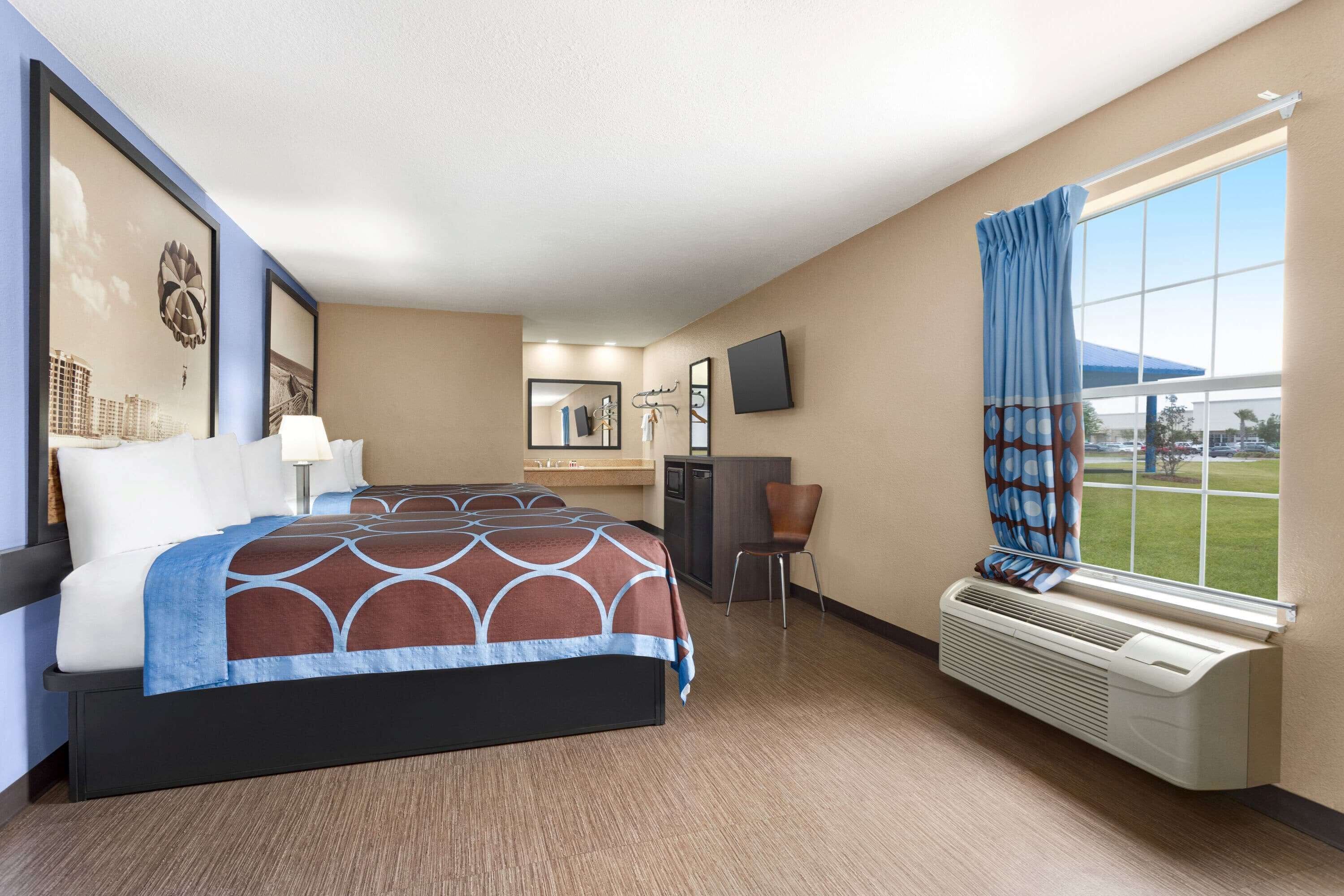 Habitación de hotel con cama, escritorio, silla, ventana con cortinas y televisor montado en la pared.