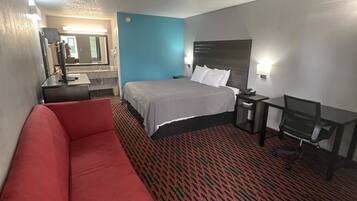A hotel room with a bed, a red sofa, a desk, a chair, a mirror, and a patterned carpet.