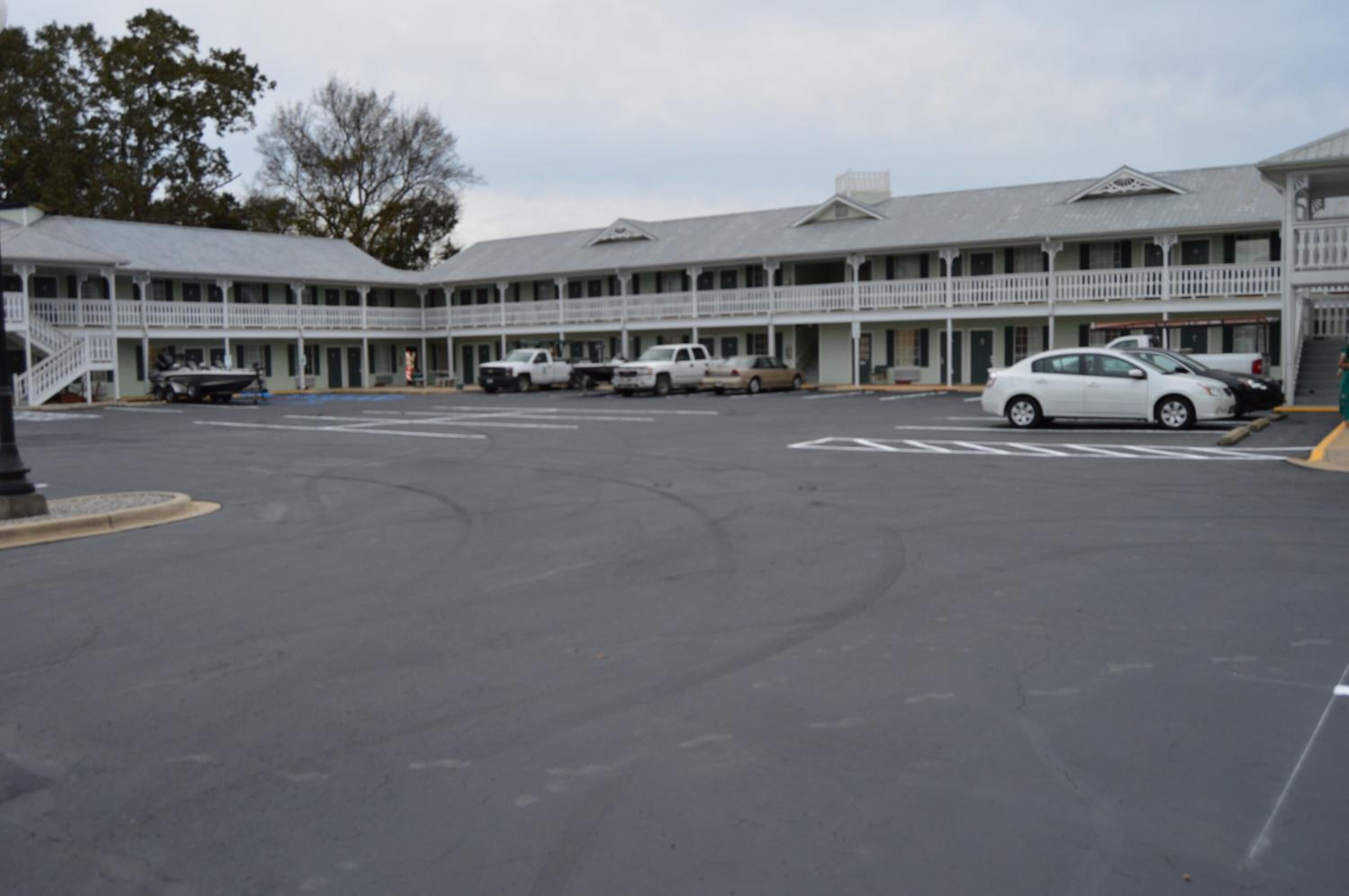 Un motel con un patio central, varios balcones y una fila de coches aparcados.