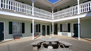 A courtyard with a central stone table and four benches, surrounded by a two-story building with balconies and large windows. - Keywest Inn - Tuscumbia/Muscle Shoals (Tuscumbia)
