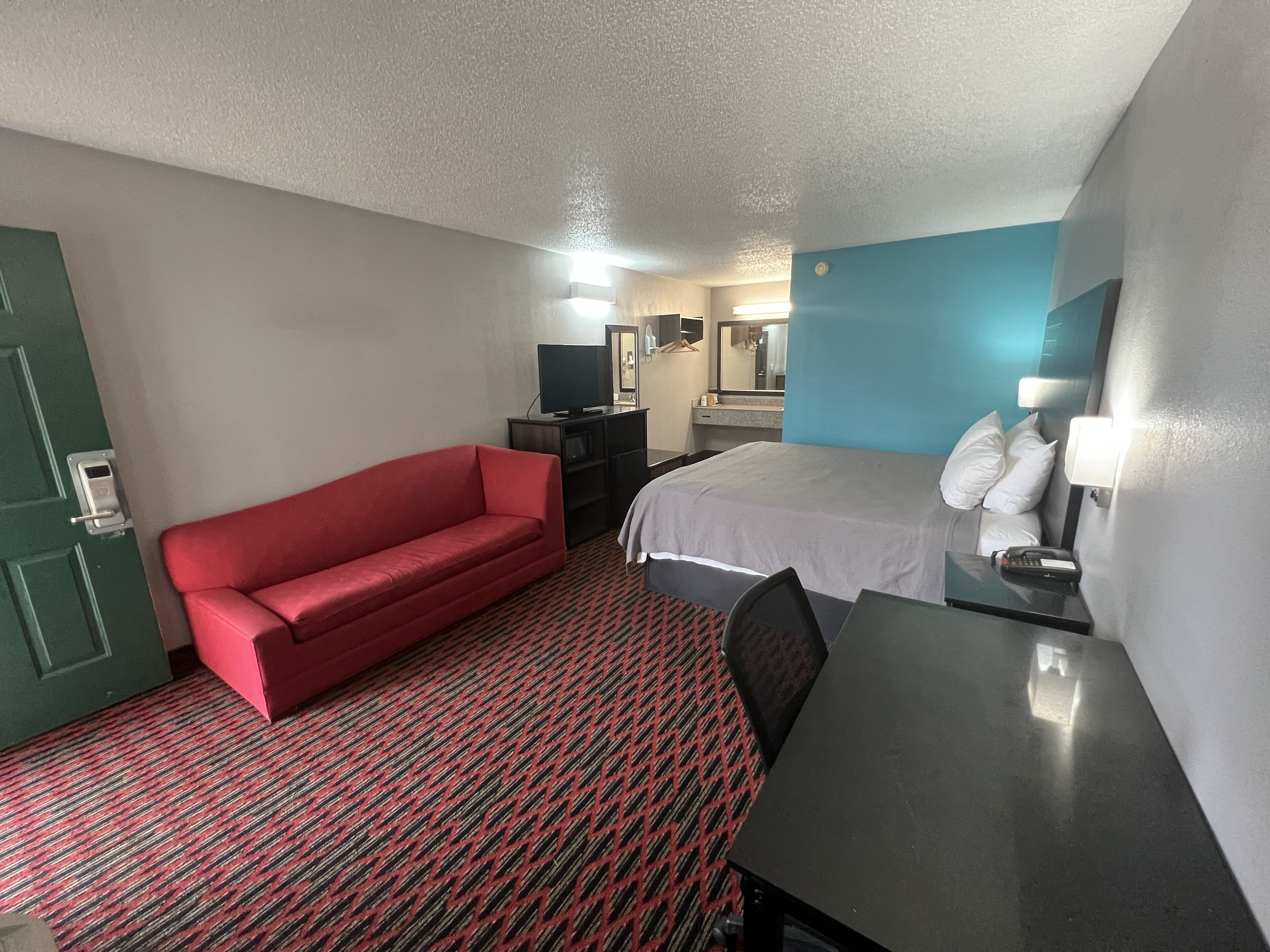 A hotel room with a red sofa, a bed, a desk, a TV, and a mirror.