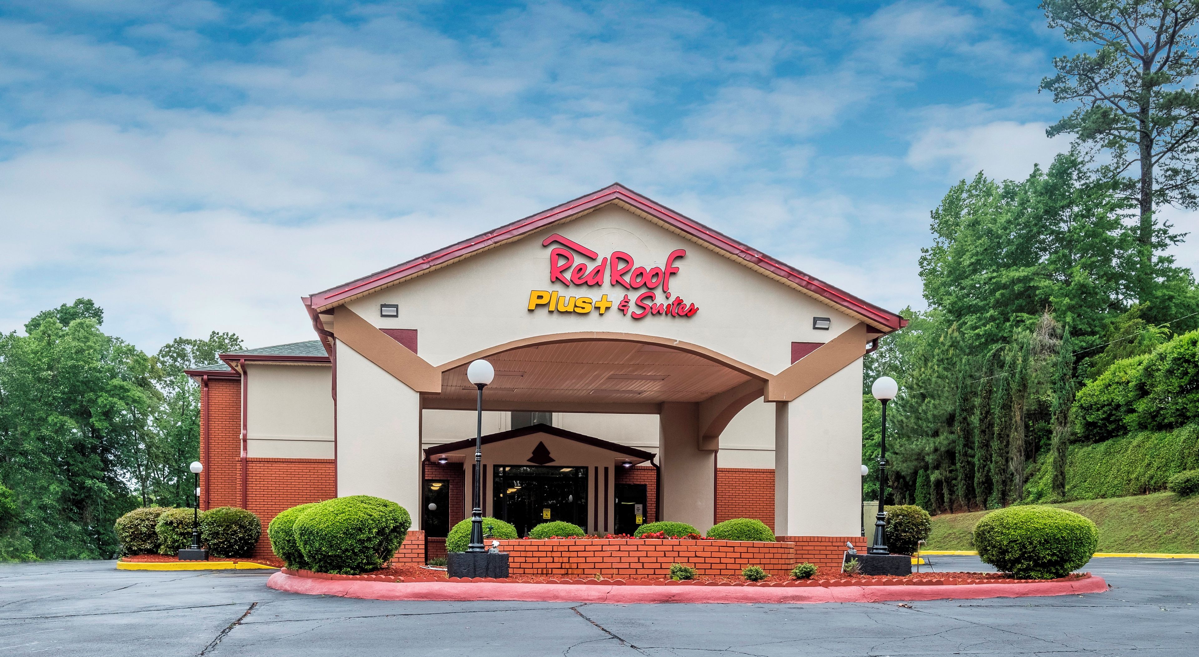 A Red Roof Plus Suites hotel with a covered entrance, brick facade, and landscaped surroundings.
