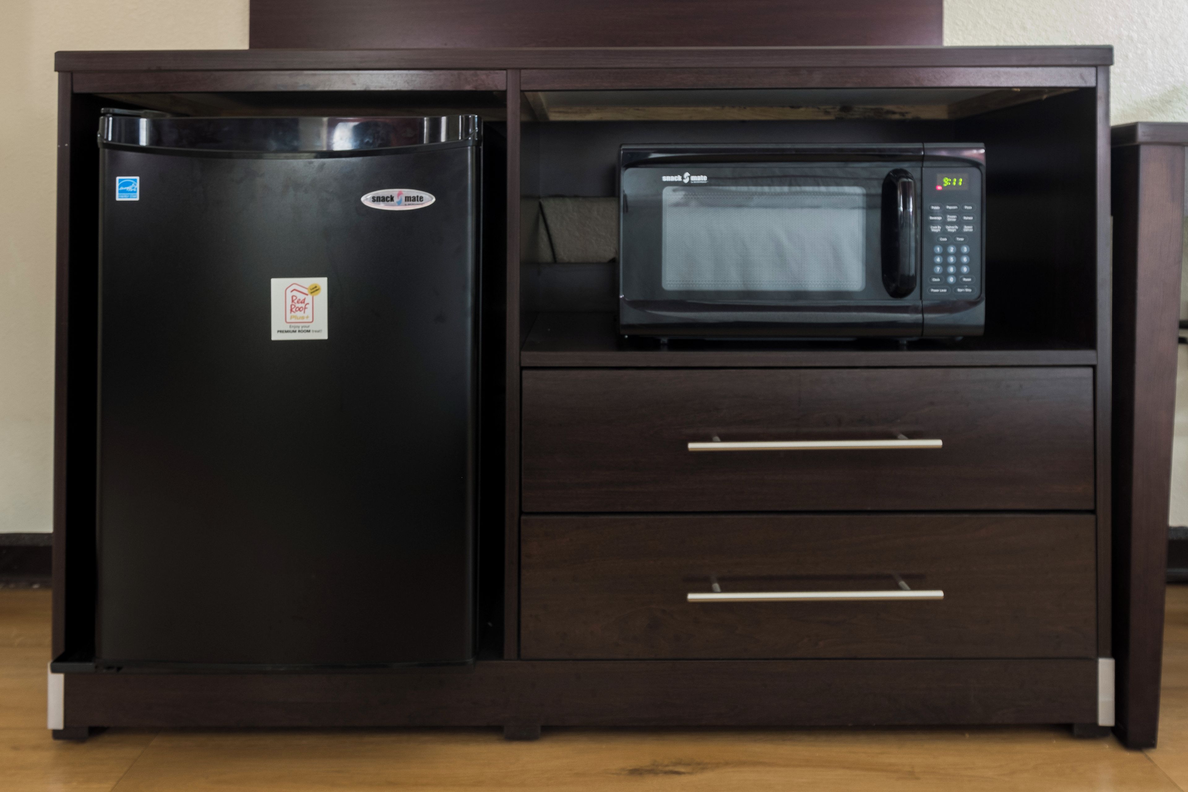 A kitchenette with a black refrigerator and a microwave on top.