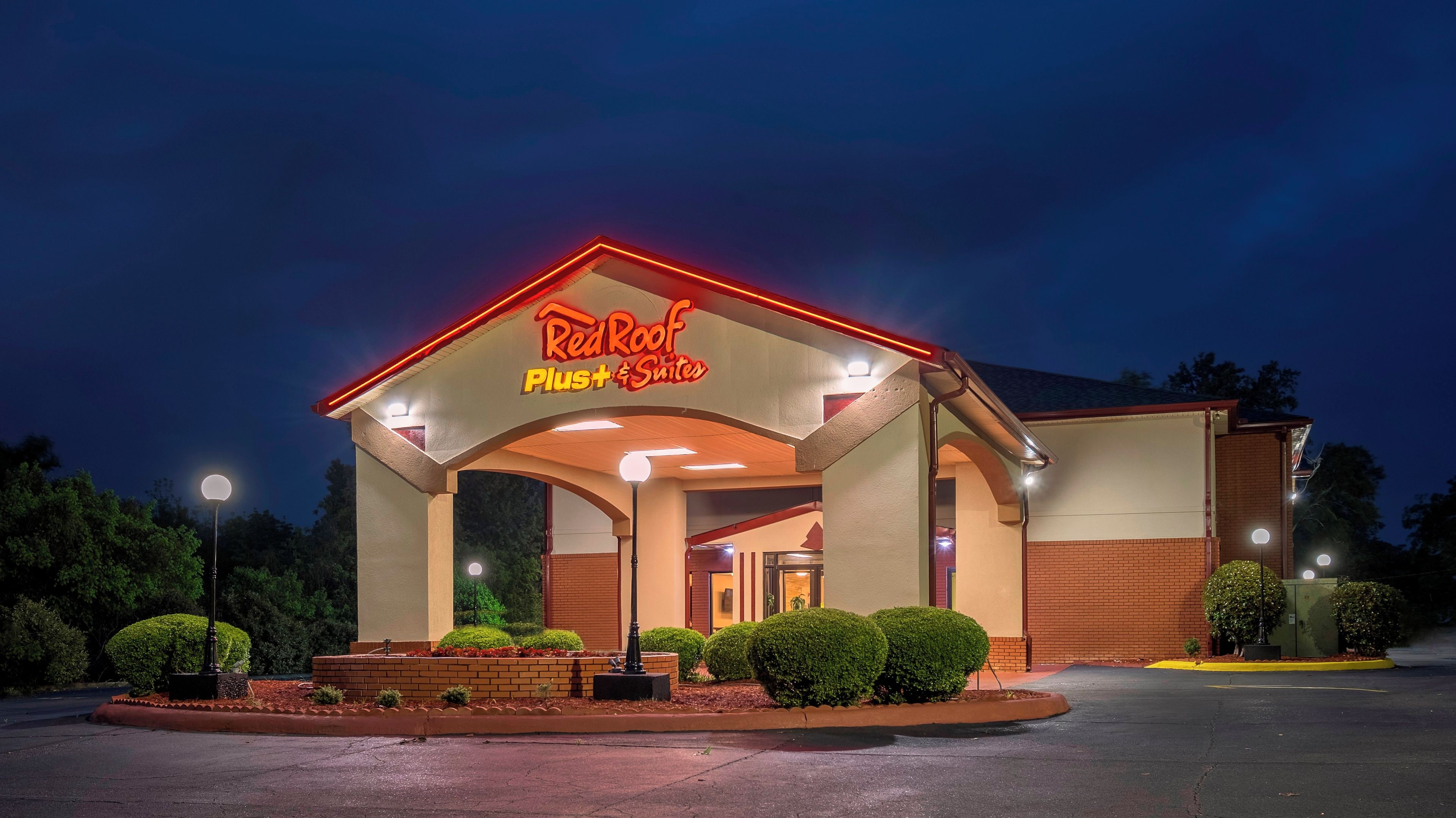 A Red Roof Plus Suites hotel with a covered entrance, well-lit signage, and landscaped front yard.