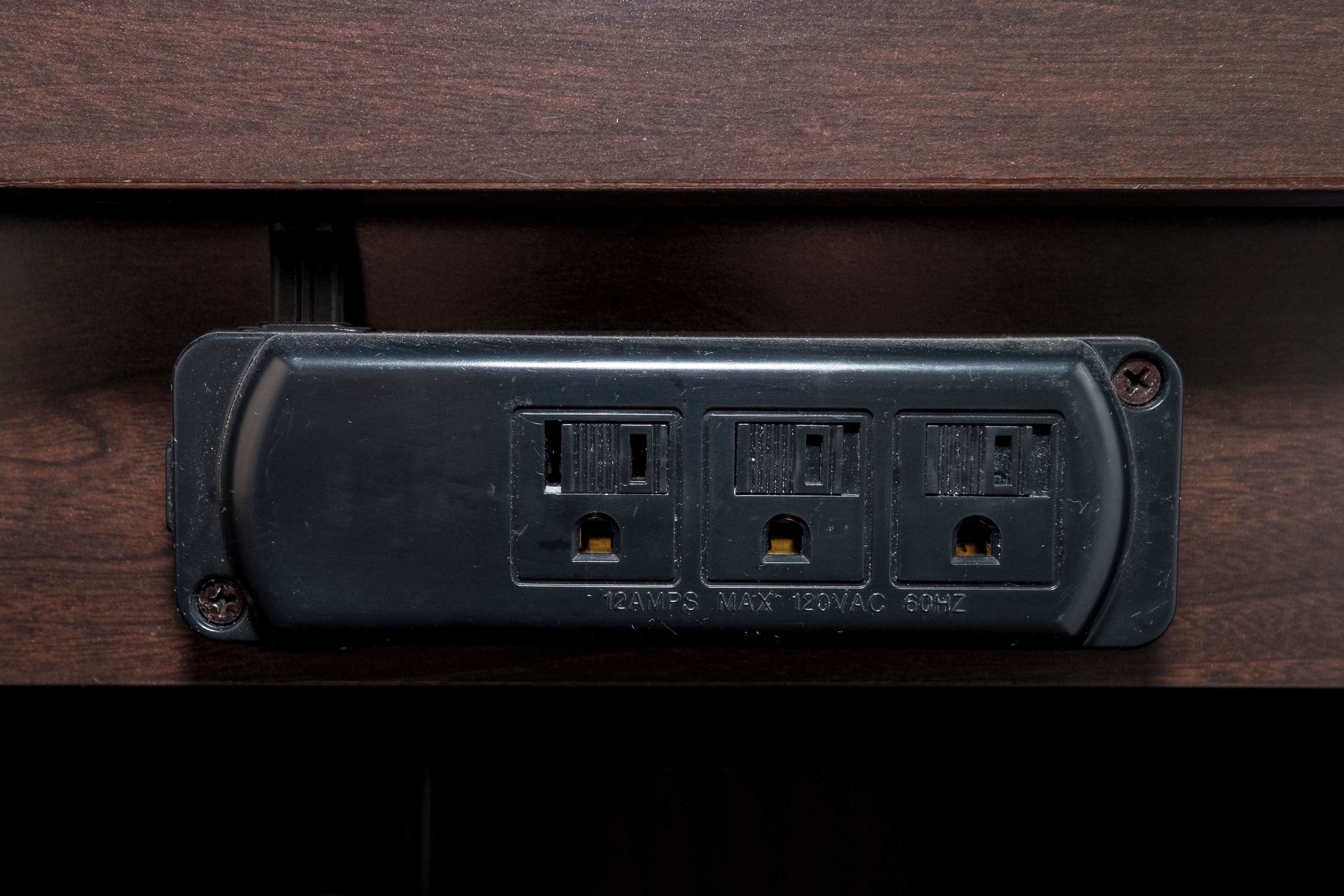 A wall-mounted electrical outlet with three sockets, a switch, and a grounding screw.
