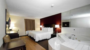 Una camera d'albergo con un letto, una scrivania, una sedia, uno specchio grande, un bagno con una vasca e una finestra con tende.
