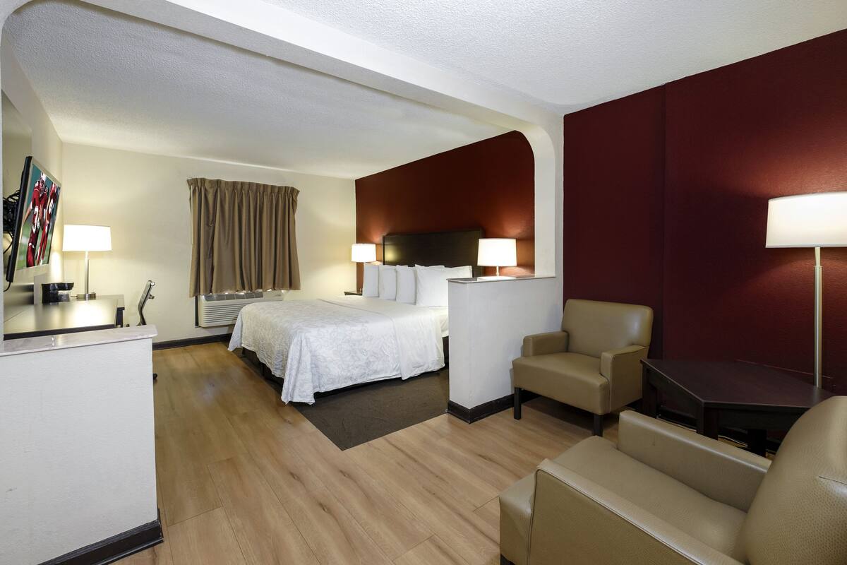 A hotel room with a bed, two bedside tables, a desk, a chair, and a sofa.