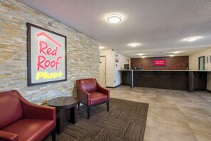 A Red Roof Plus hotel lobby with a stone wall, a reception desk, and leather chairs. - Red Roof Inn PLUS+ & Suites Opelika (Opelika)