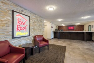 A Red Roof Plus hotel lobby with a stone wall, a reception desk, and leather chairs.