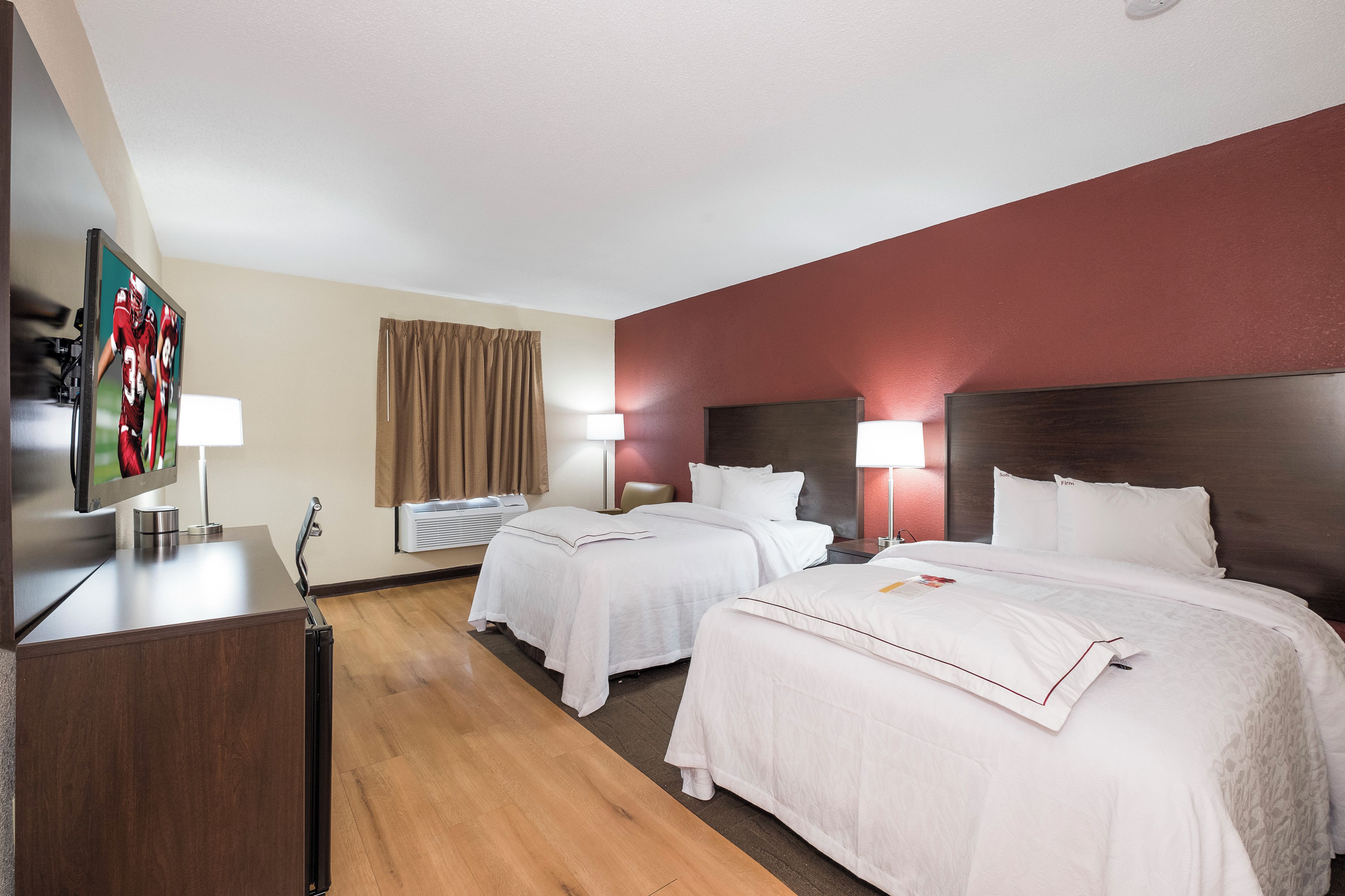 A hotel room with two beds, a desk, a television, and a window with curtains.