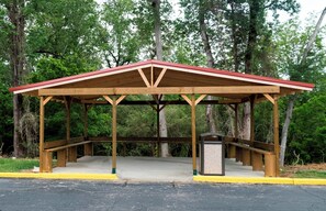 A wooden pavilion with a red roof, a concrete floor, and a trash can. - Red Roof Inn PLUS+ & Suites Opelika (Opelika)