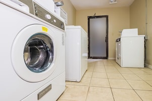 Un cuarto de lavado con lavadora y secadora de carga frontal, un refrigerador pequeño y una puerta que da a otra habitación.