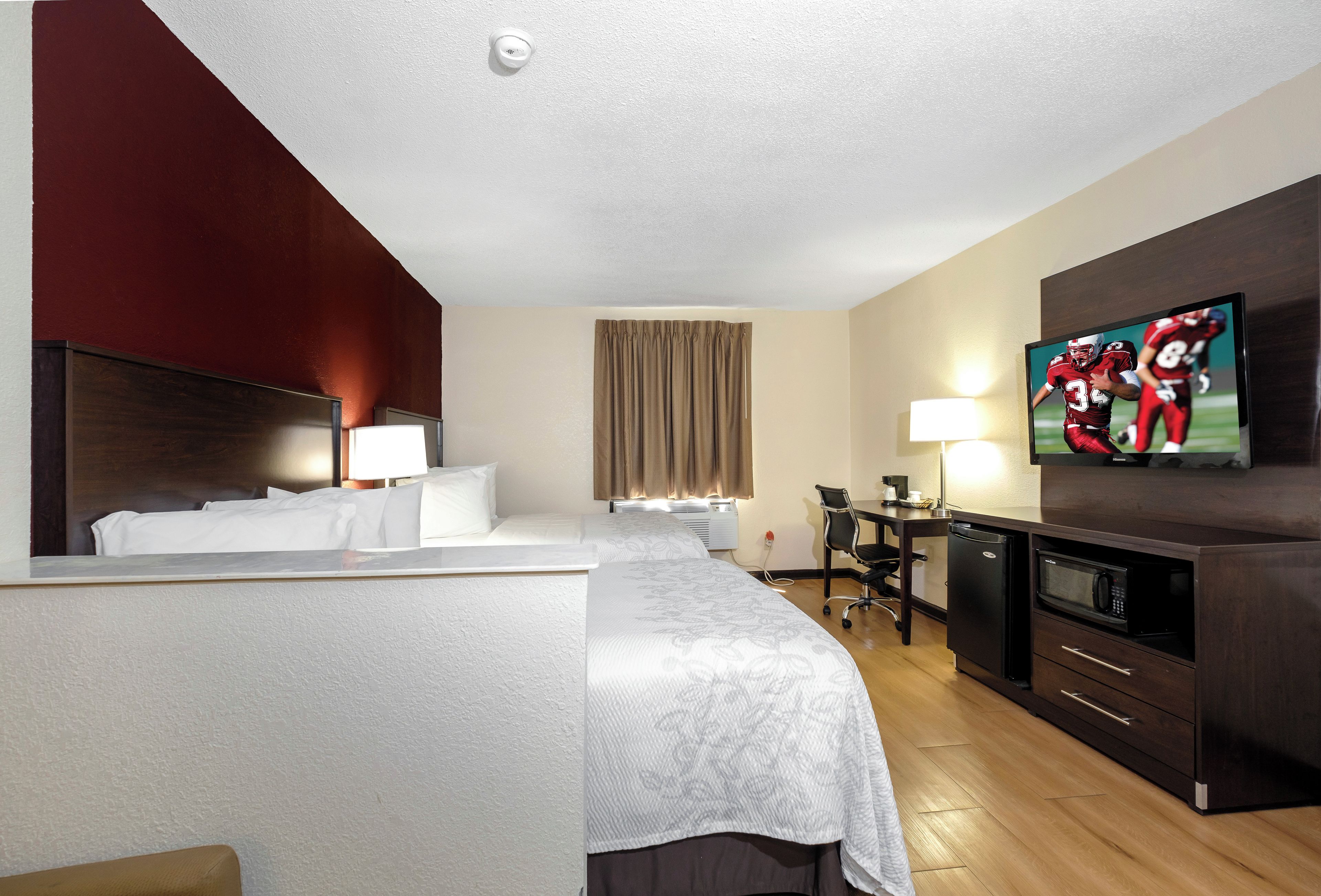 A hotel room with a bed, bedside tables, a desk with a chair, a television, and a microwave.