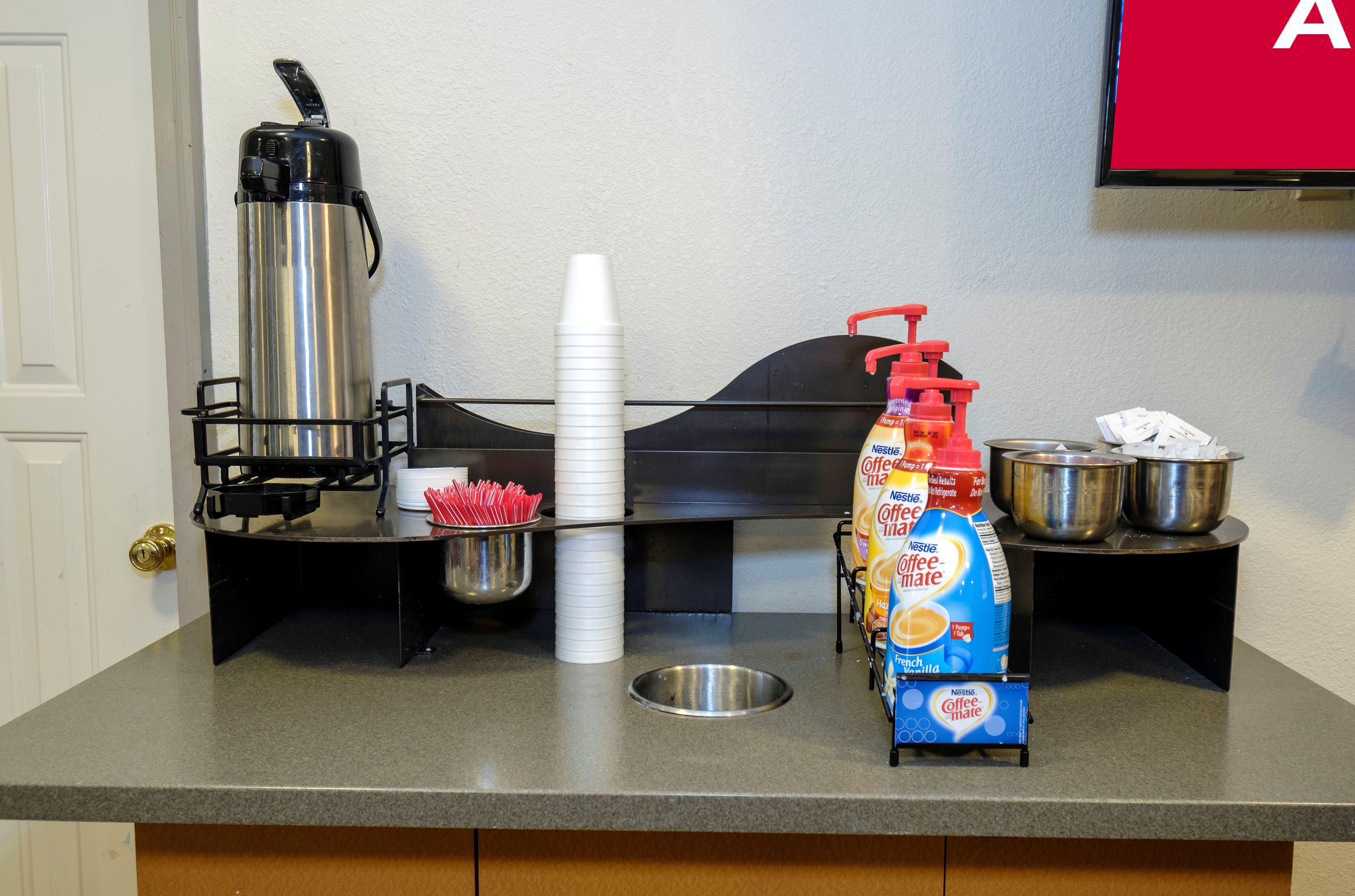 A kitchenette with a coffee maker, a bottle of coffee creamer, a metal bowl, and a stack of white cups.