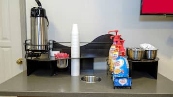 A kitchenette with a coffee maker, a bottle of coffee creamer, a metal bowl, and a stack of white cups.