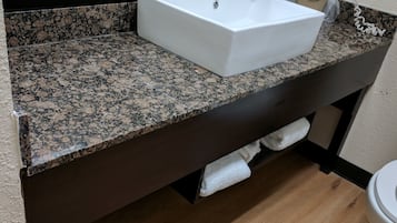 A bathroom with a granite countertop, a white sink, and a toilet.