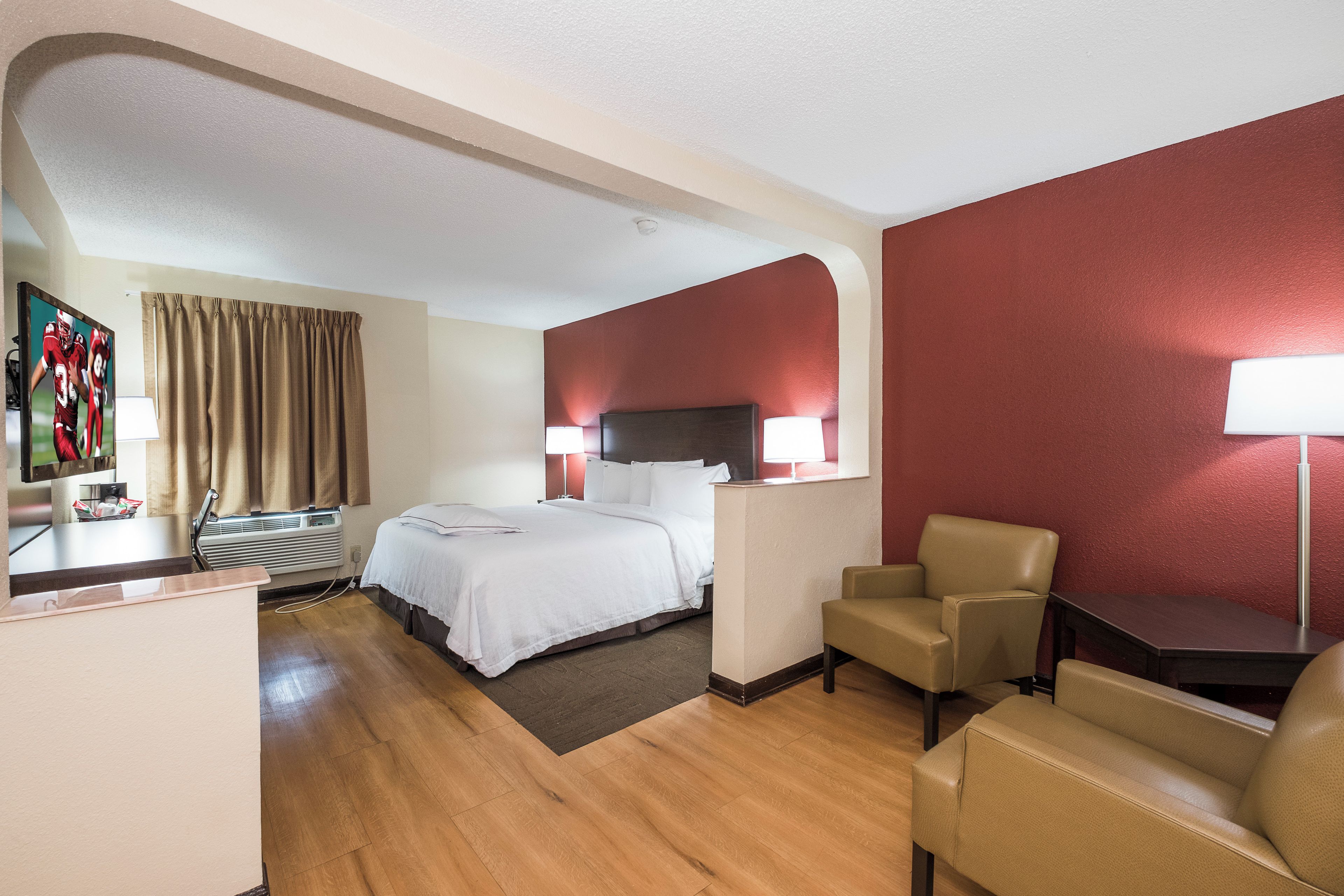Habitación de hotel con cama, dos lámparas de noche, escritorio con silla, televisor y ventana con cortinas.