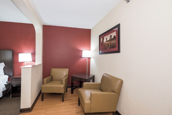 Una habitación de hotel con una cama, dos sillas, una mesita y una lámpara.