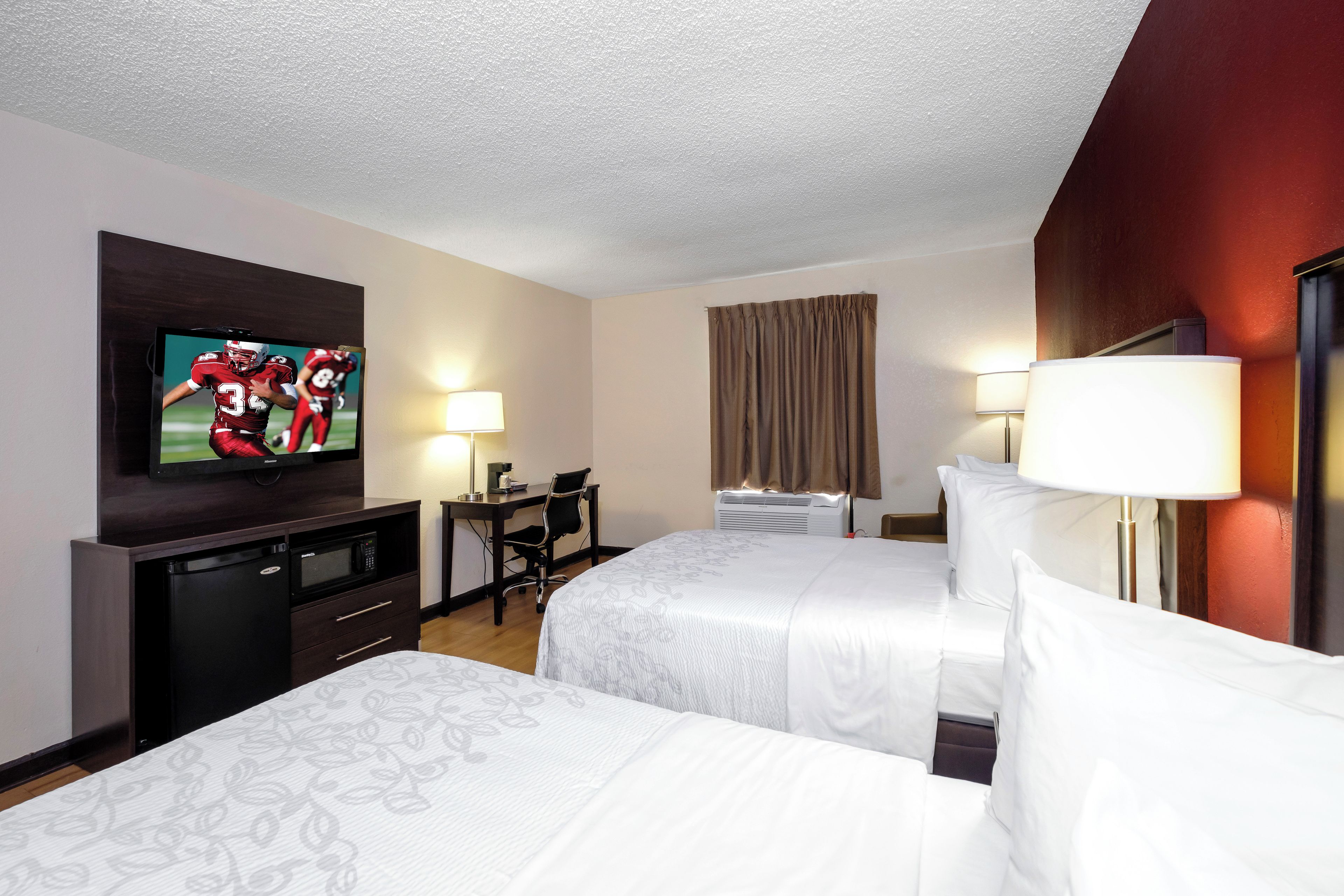 Une chambre d’hôtel avec deux lits, un bureau, une télévision, une lampe et un appareil de climatisation.