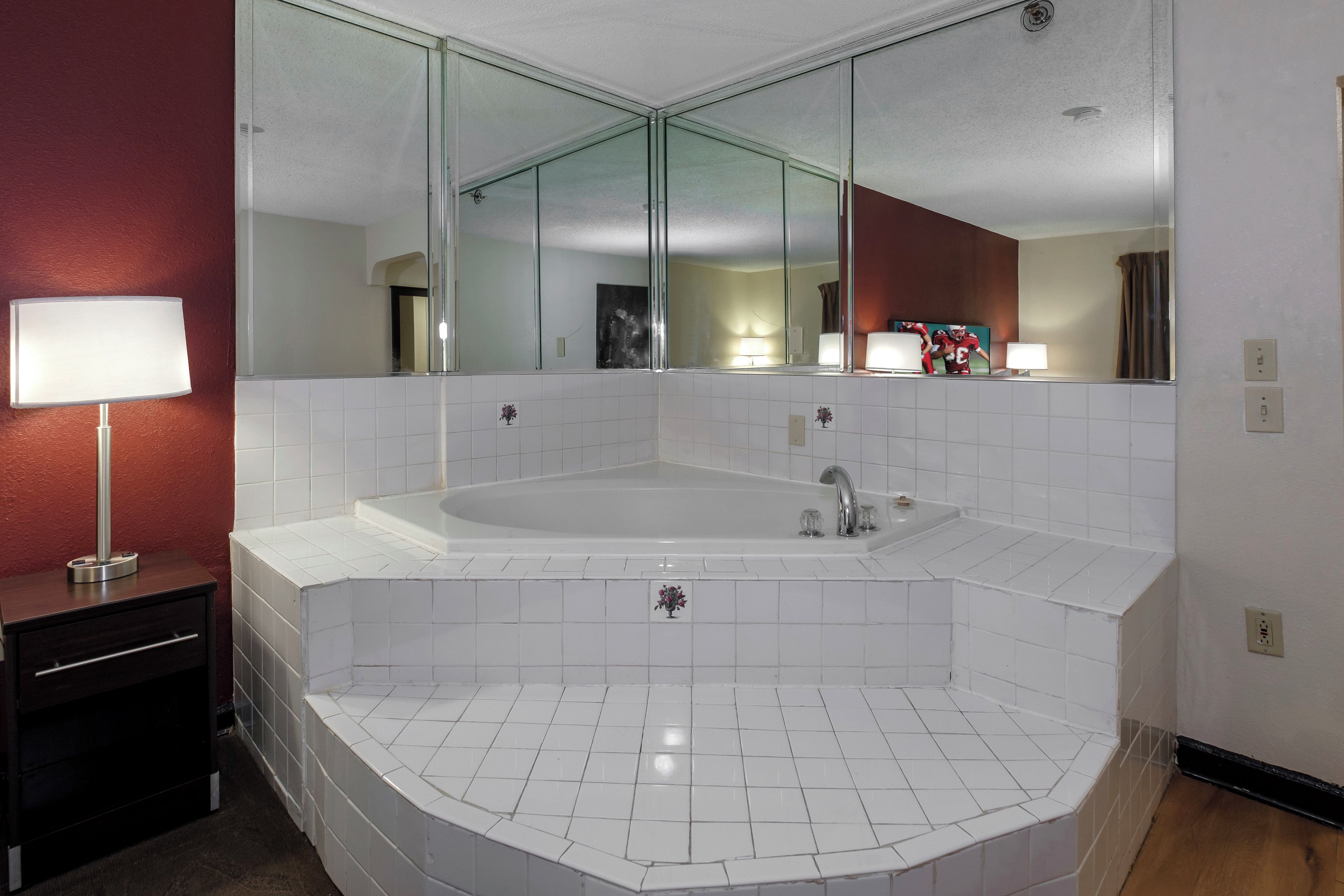 A bathroom with a large bathtub, a mirror, and a vanity with a lamp.