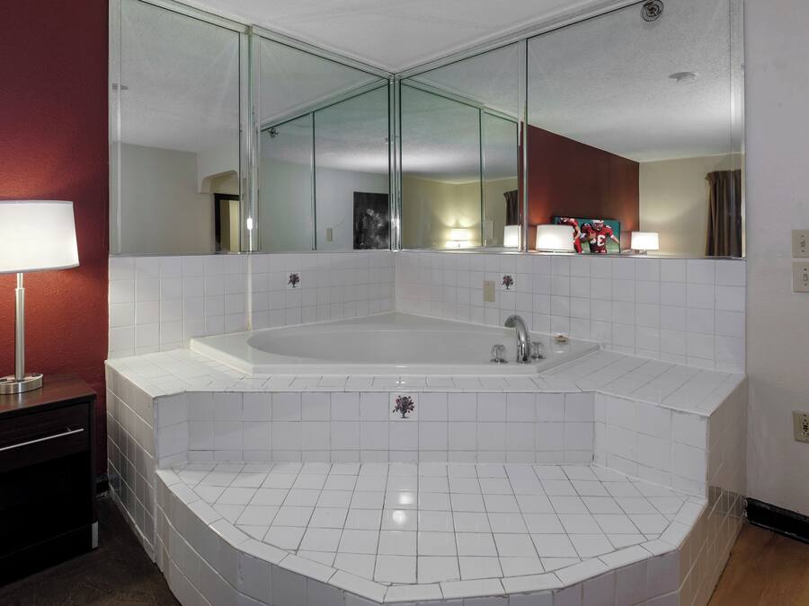 A bathroom with a large bathtub, a mirror, and a vanity with a lamp.