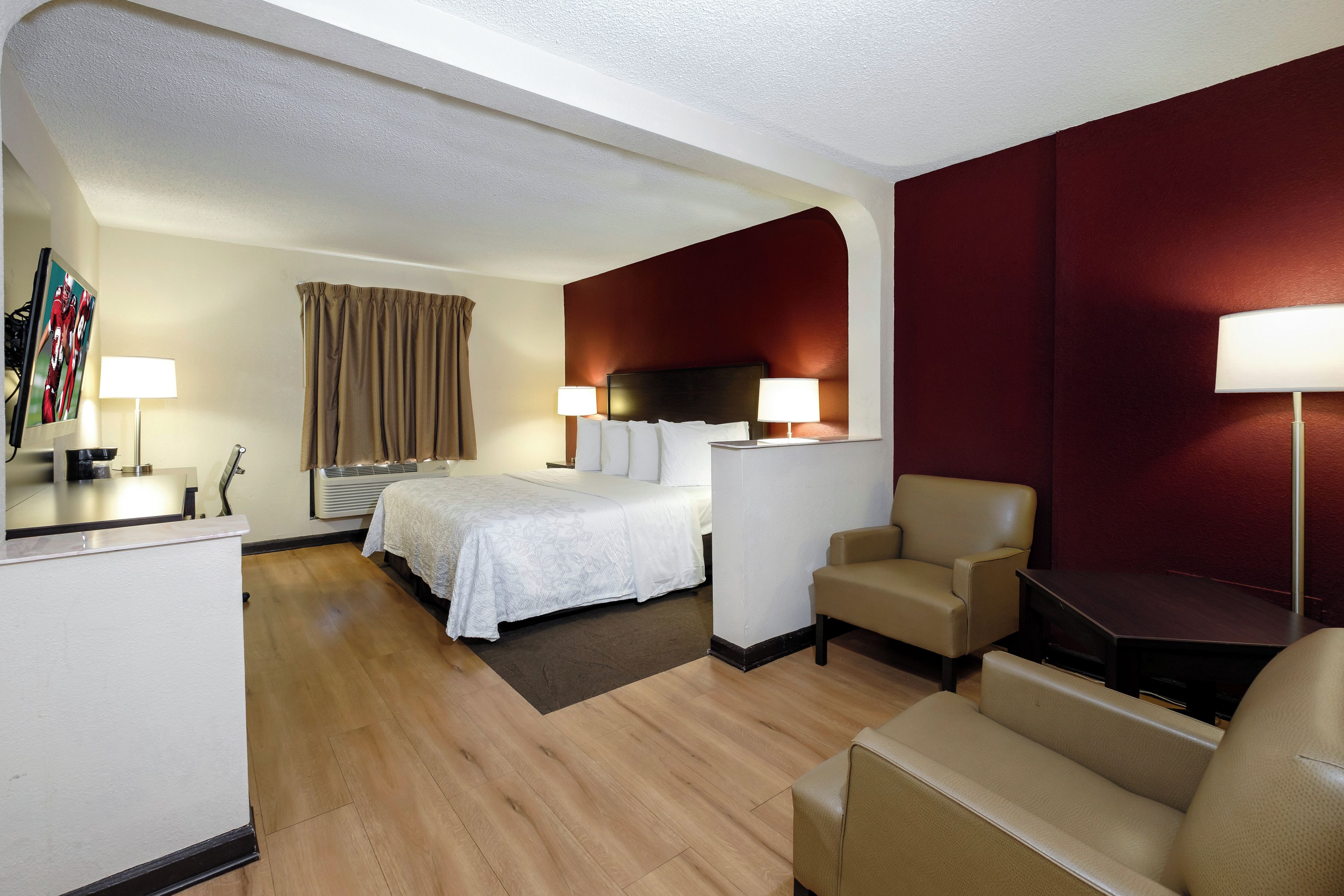 Une chambre d’hôtel comprenant un lit, deux tables de chevet, un bureau, une chaise, un canapé et un mur d’accent de couleur rouge.