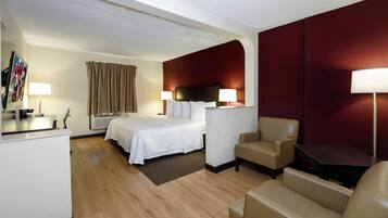 Une chambre d’hôtel comprenant un lit, deux tables de chevet, un bureau, une chaise, un canapé et un mur d’accent de couleur rouge.