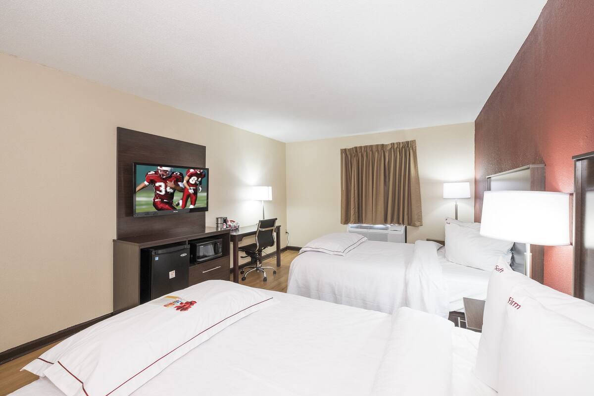 A hotel room with two beds, a desk with a computer, a TV, and a window with curtains.