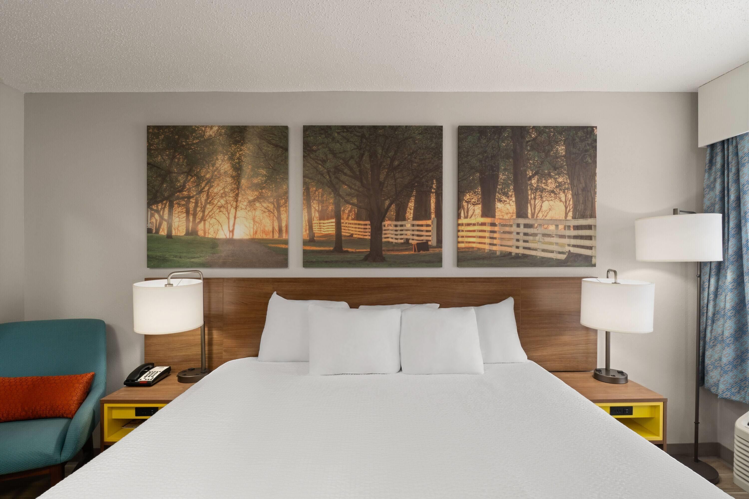 Une chambre d’hôtel avec un grand lit, deux tables de chevet avec des lampes, une chaise et trois tableaux au mur.