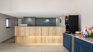 A reception area with a Days Inn sign, a wooden reception desk, a kitchen counter with cleaning supplies, and a refrigerator. - Days Inn by Wyndham Clanton AL (Clanton)