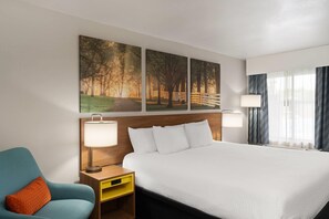 A hotel room with a large bed, two bedside lamps, a nightstand, a chair, and a painting of a forest scene.