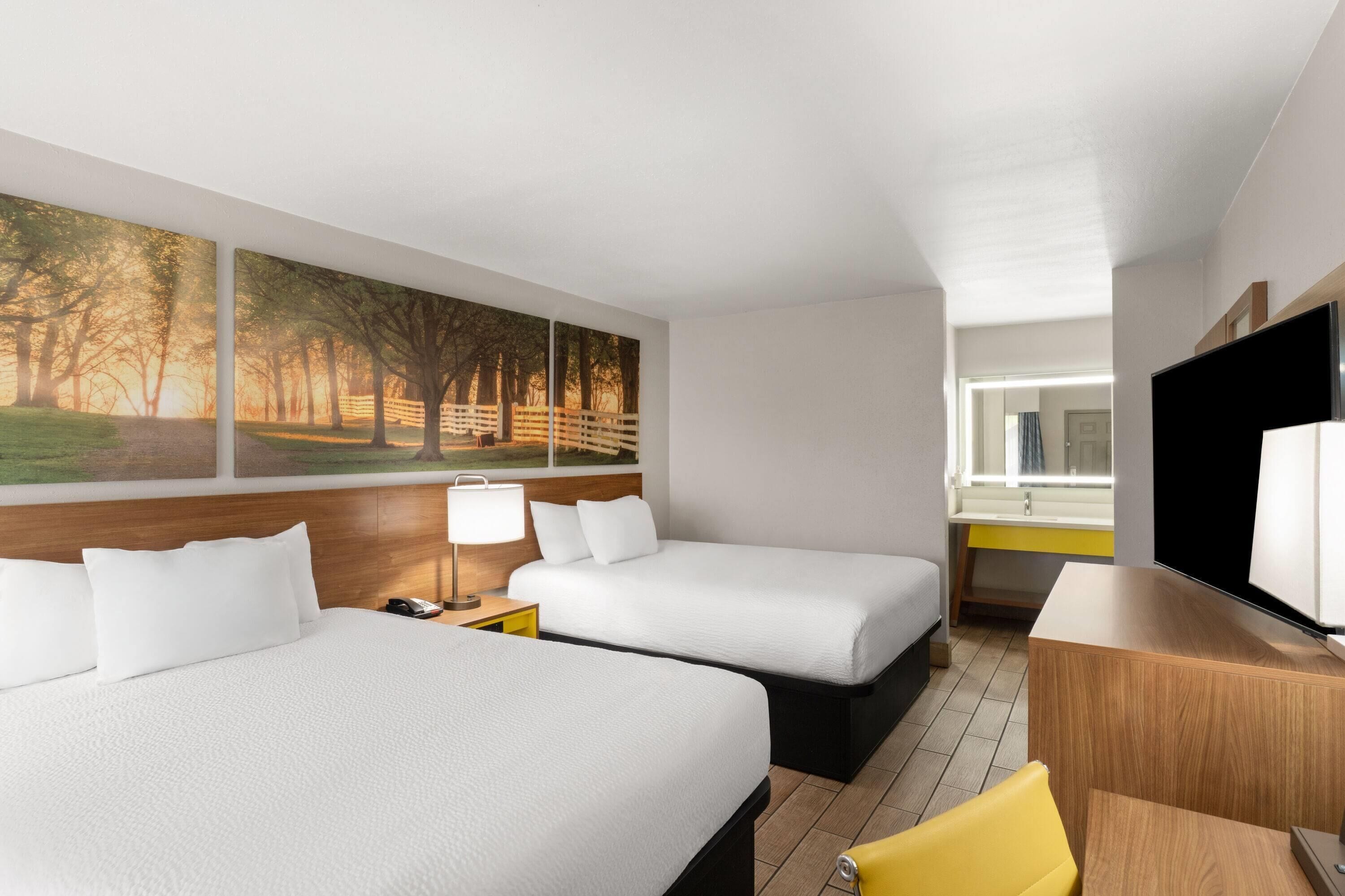 A hotel room with two beds, a desk, a chair, a TV, and a painting on the wall.