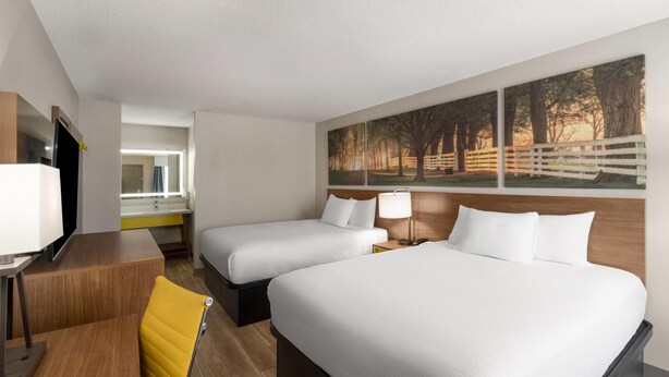 A hotel room with two beds, a desk, a chair, a TV, and a painting on the wall. - Days Inn by Wyndham Clanton AL (Clanton)