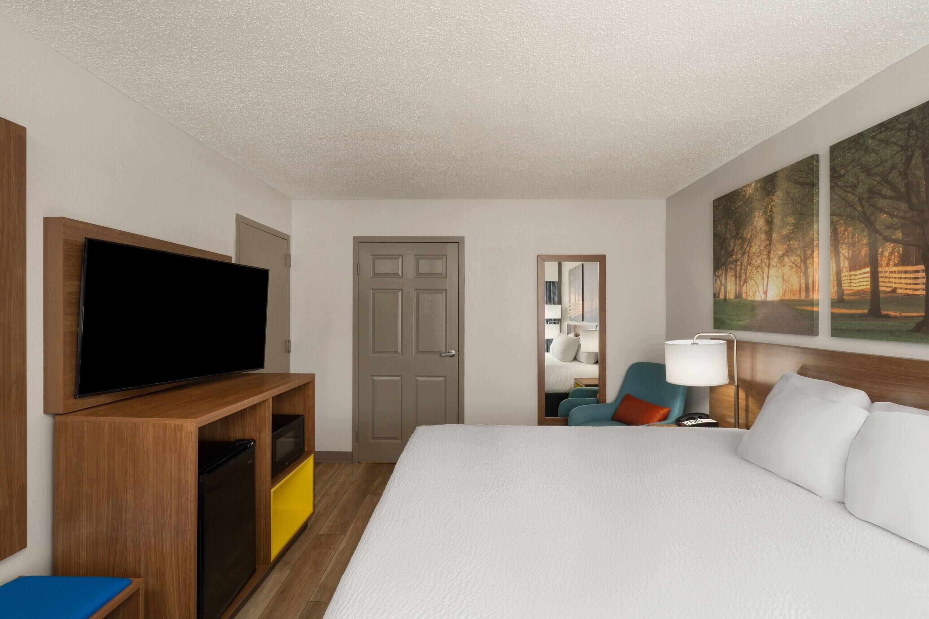 A hotel room with a bed, TV, wooden entertainment unit, and a painting on the wall.