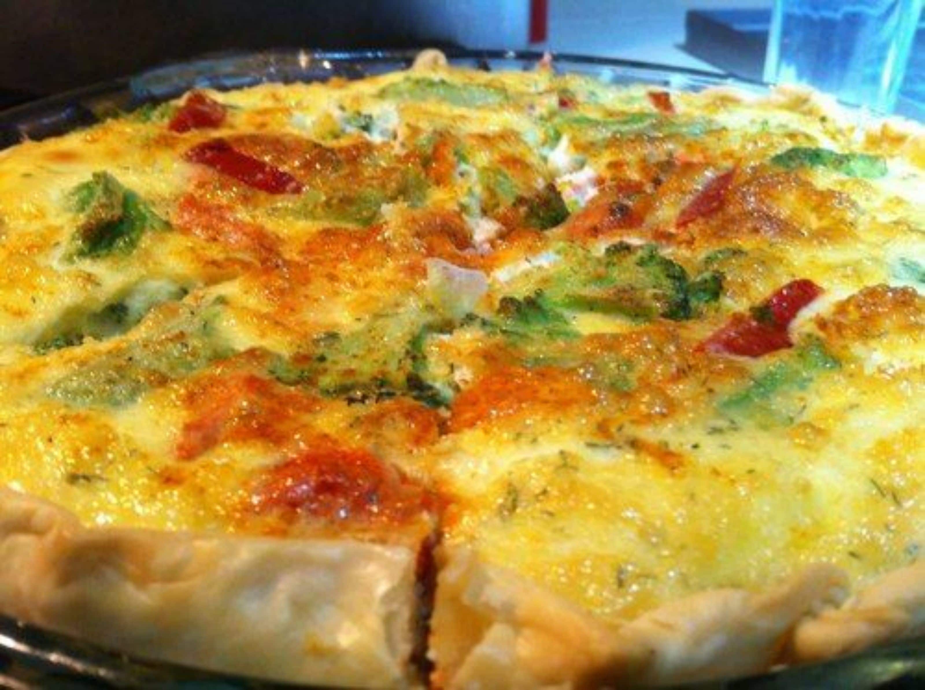 Pizza met zichtbare toppings van broccoli en rode paprika op een glazen bord.