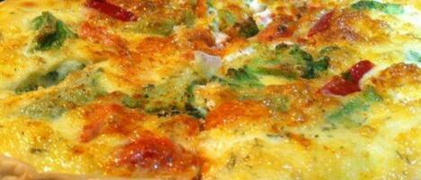 Pizza met zichtbare toppings van broccoli en rode paprika op een glazen bord.