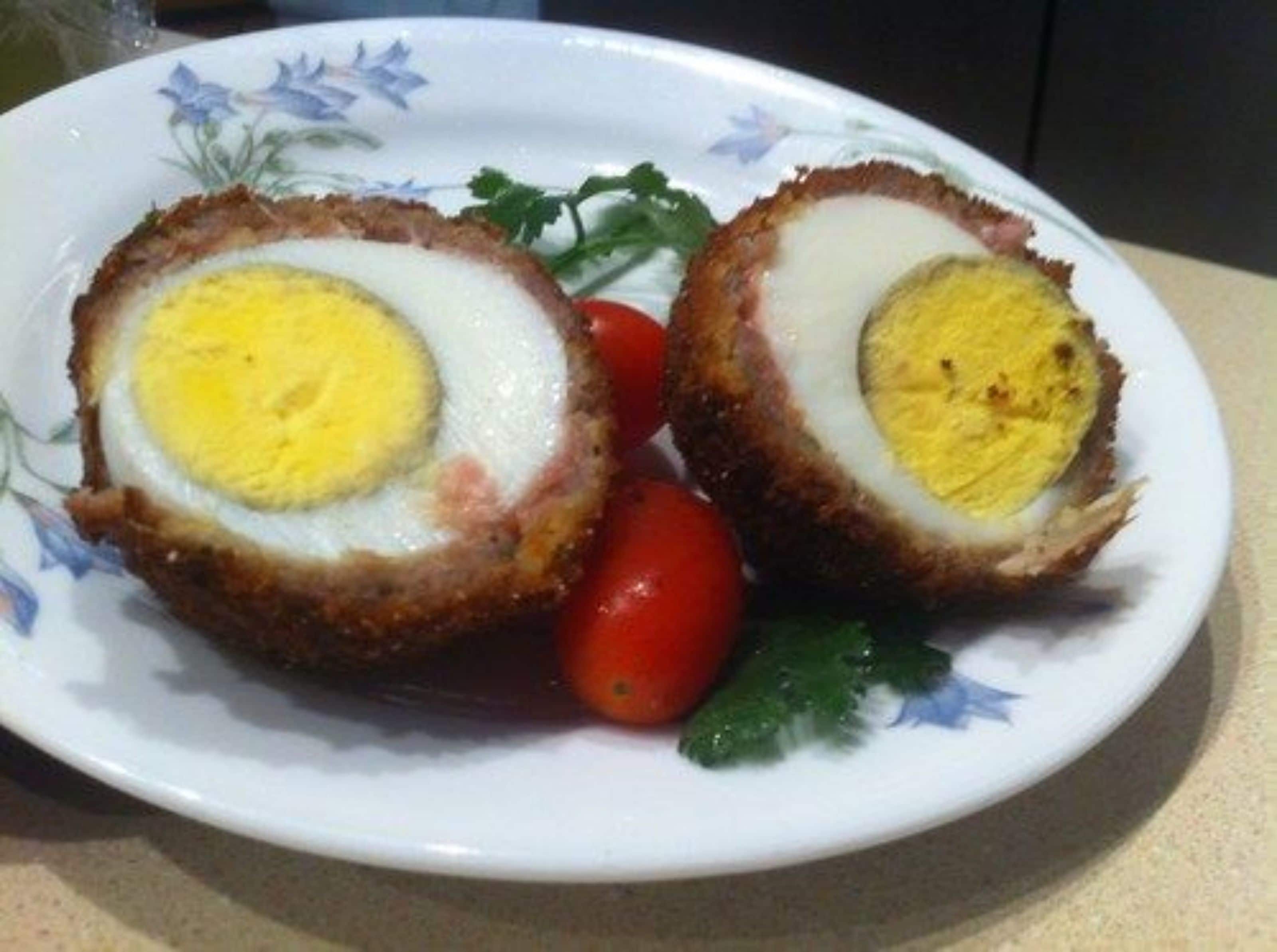 A plate with two Scotch eggs and cherry tomatoes.