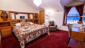 A bedroom with a large bed, wooden headboard, a desk with a chair, a window with curtains, and a chandelier. - 7 Gables Inn & Suites (Fairbanks)