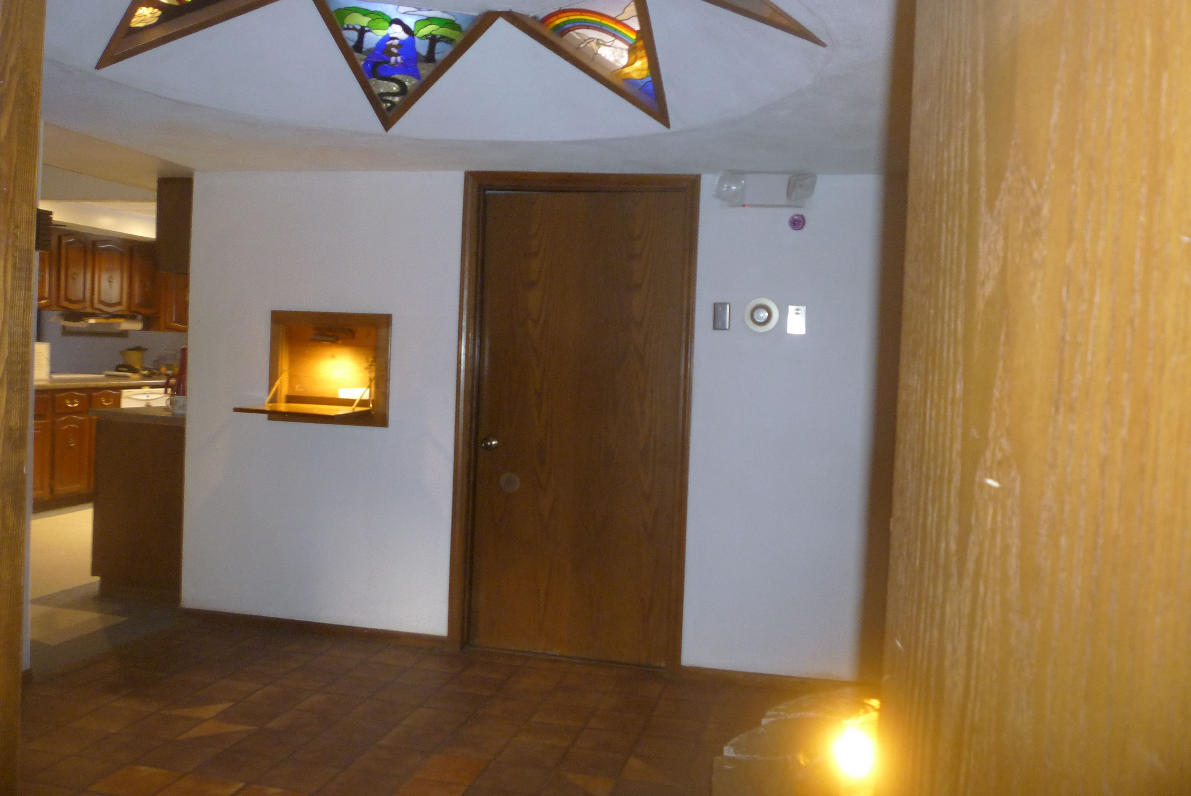 A hallway with a wooden door, a small window with a light, and a tiled floor.