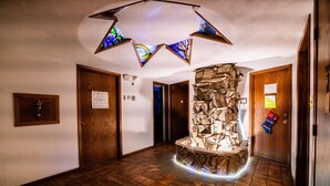 A hallway with a stone fireplace, wooden doors, and a stained glass ceiling. - 7 Gables Inn & Suites (Fairbanks)