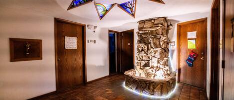 Un couloir agrémenté d’une cheminée en pierre, de portes en bois et d’un plafond orné de vitraux.