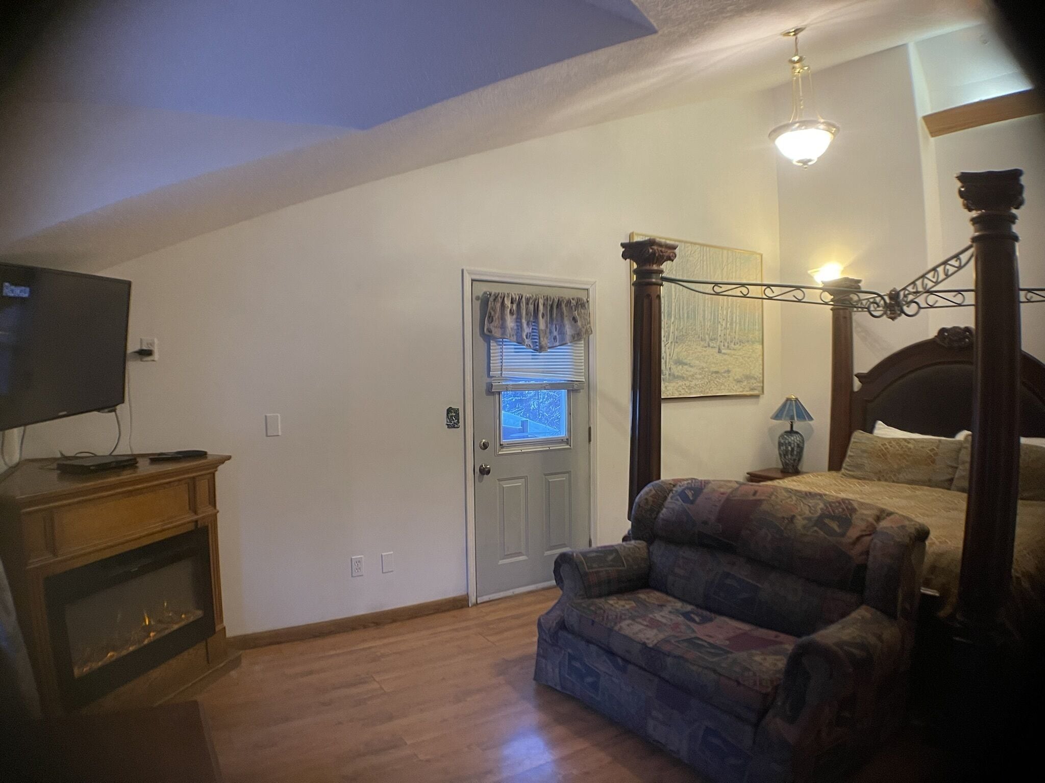 Un dormitorio con una cama con dosel, un televisor sobre un mueble y una puerta con ventana.