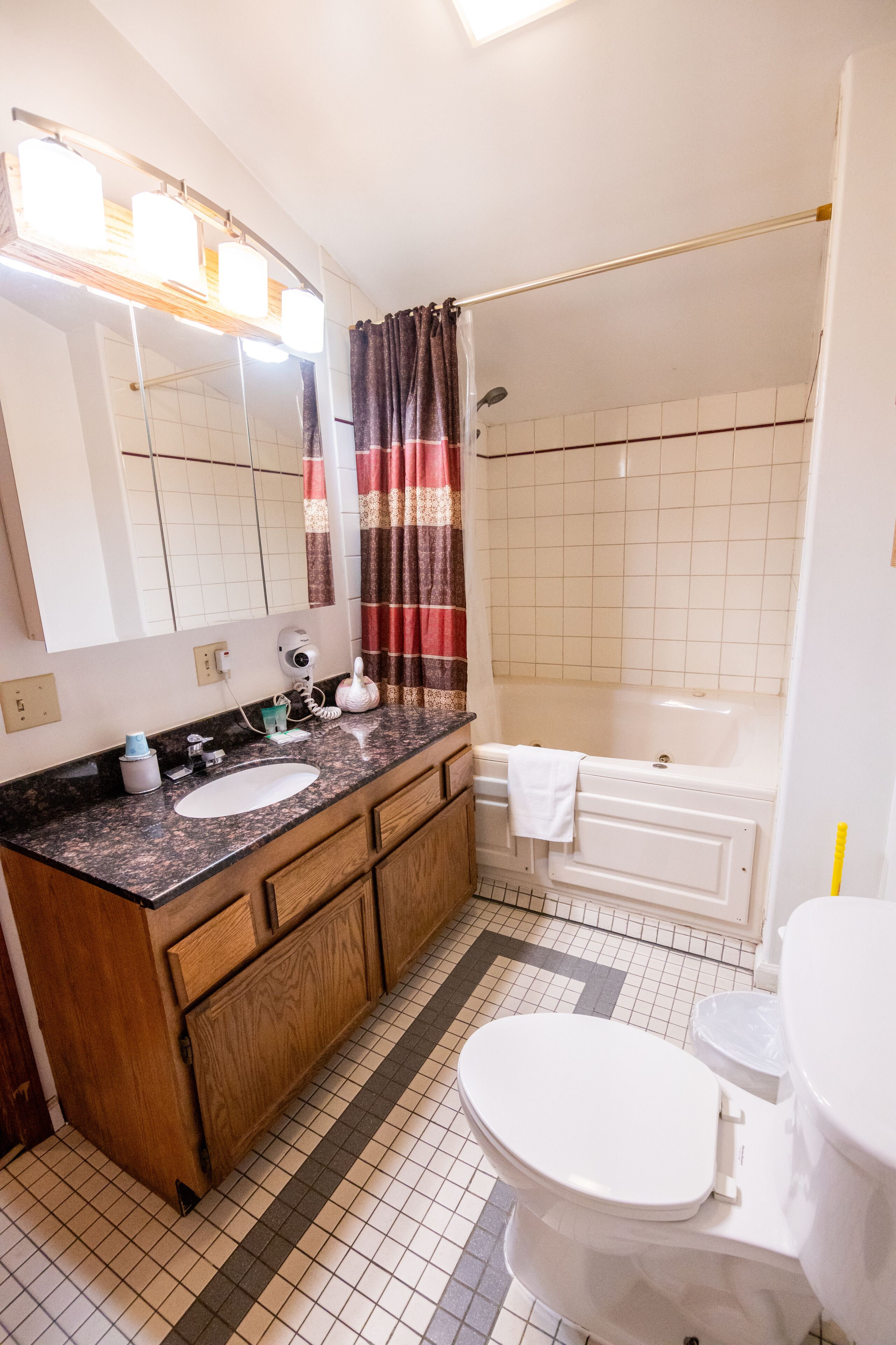 Un baño con lavamanos, espejo, tocador, inodoro, bañera y cortina de ducha.
