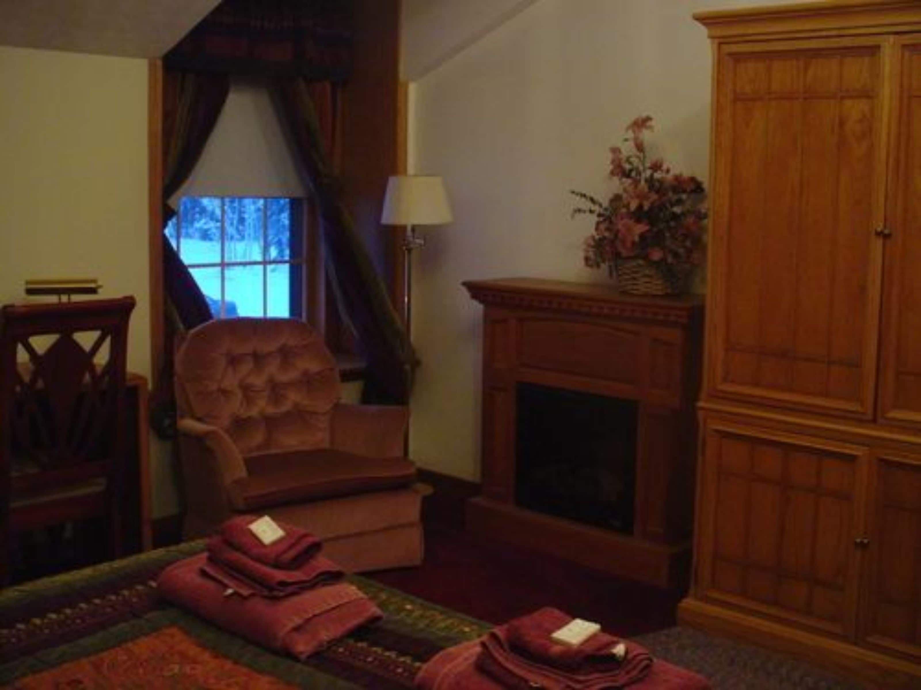 Una habitación con chimenea, un armario de madera grande, una silla y una cama con mantas dobladas.