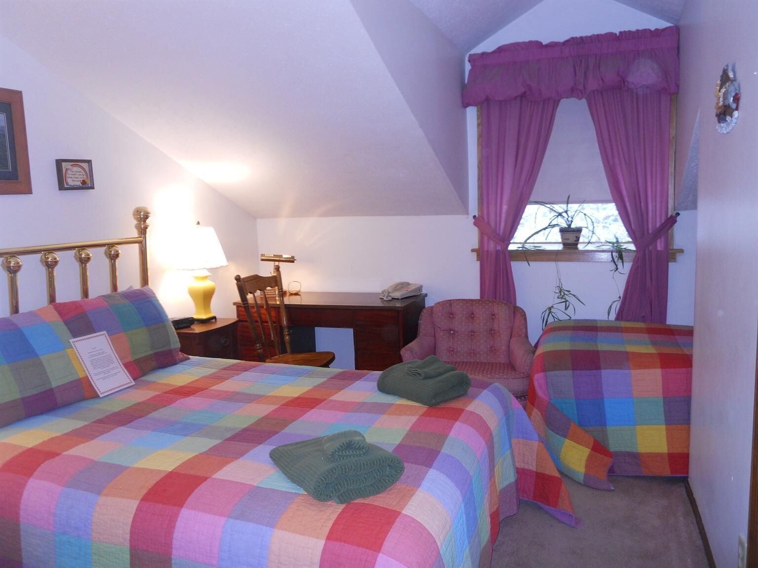 Une chambre avec deux lits, un bureau, une chaise et une fenêtre avec des rideaux.