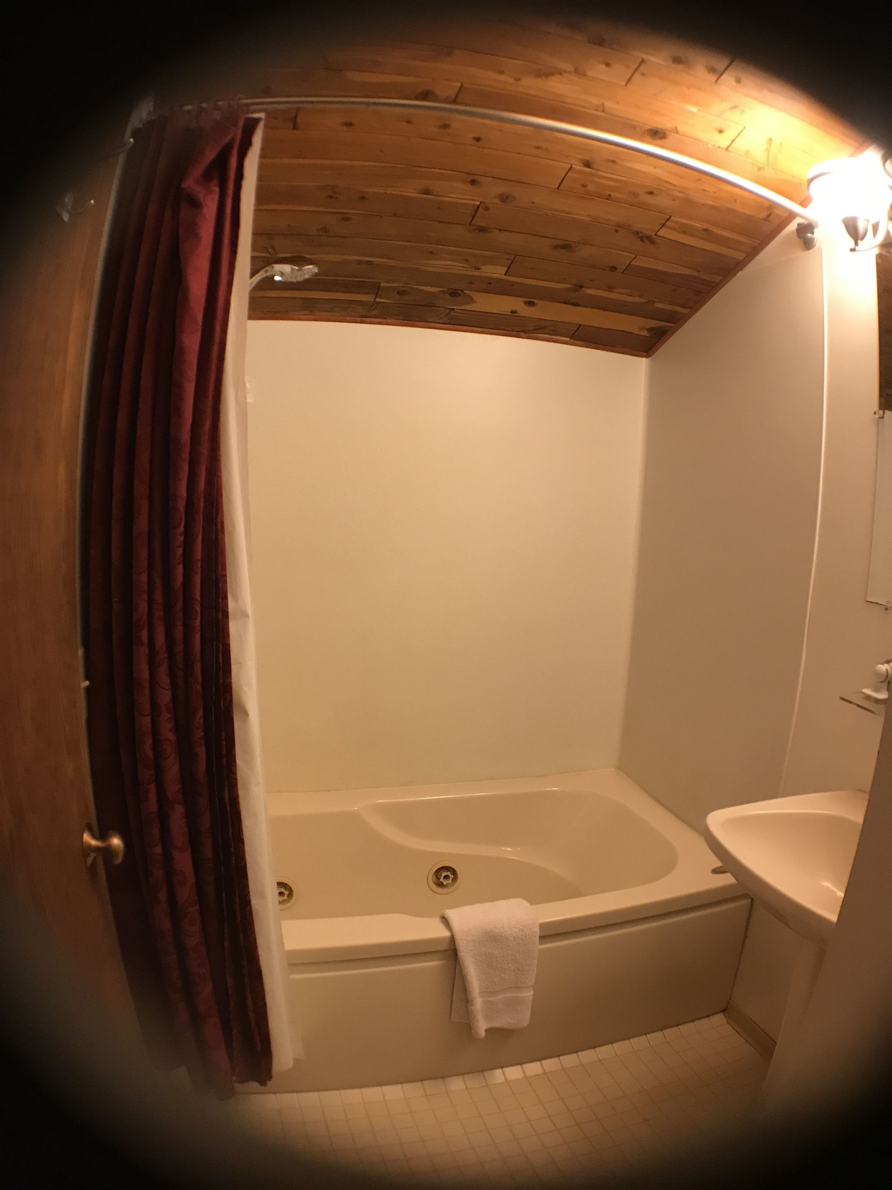 Un baño con techo de madera, una bañera y un lavamanos.
