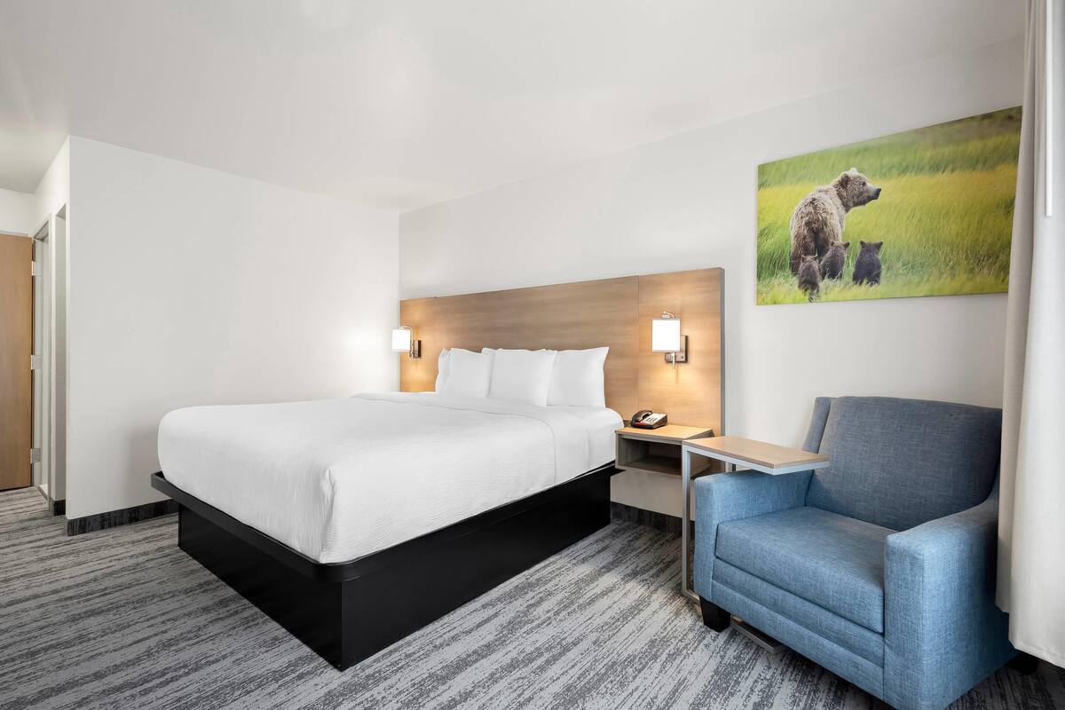 A hotel room with a bed, bedside tables, a chair, and a painting on the wall.