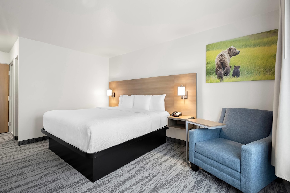 A hotel room with a bed, bedside tables, a chair, and a painting on the wall.