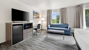 Una habitación de hotel con cama, televisión, escritorio y silla, sofá y ventana con cortinas.