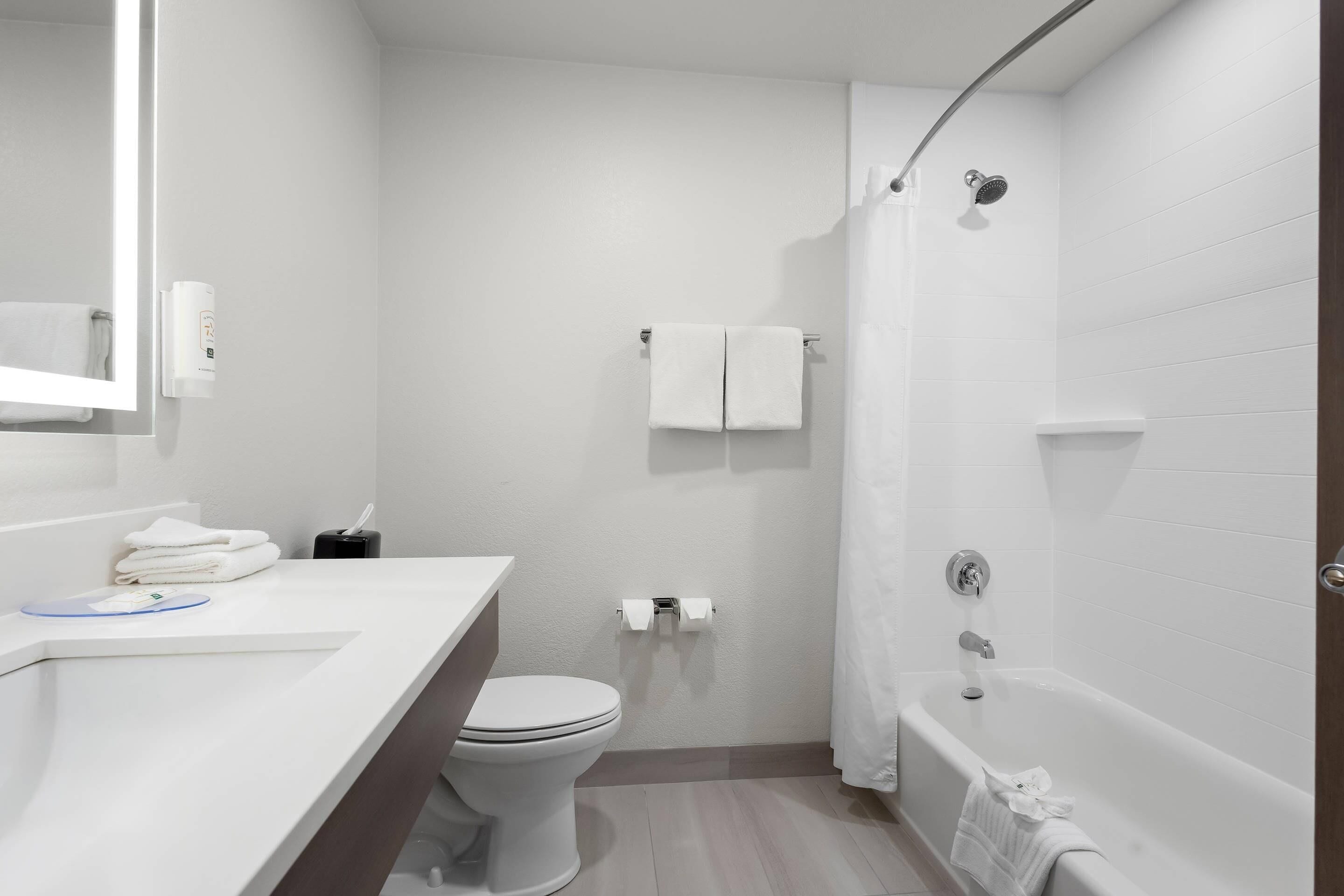 A modern bathroom with a white sink, toilet, and bathtub. There is a towel rack with two towels and a toilet paper holder.